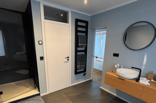 Modernes Badezimmer mit Waschbecken, Wandspiegel und Zugang zur Dusche.