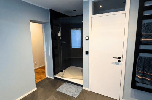 Modernes Badezimmer mit Dusche, grauen Wänden und Holzfußboden.