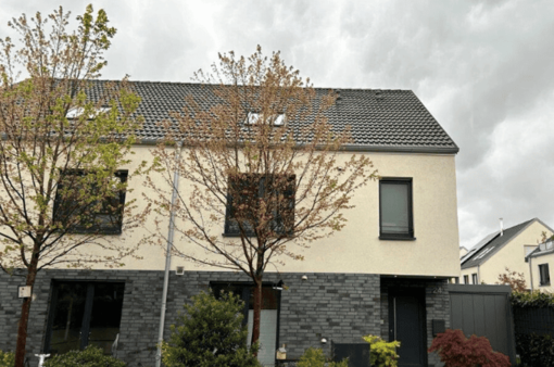 Moderne Wohnhausfassade mit großen Fenstern und Bäumen im Vordergrund. Wolkiger Himmel.