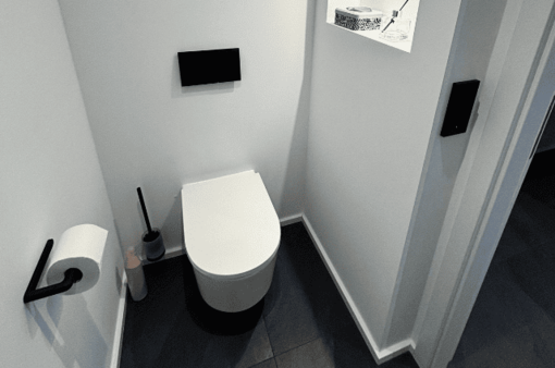 Modernes Badezimmer mit einer hängenden Toilette, Toilettenpapier und Putzutensilien.